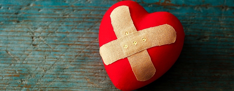 Ein rotes Herz, auf dem zwei Pflaster in Form eines Kreuzes kleben.