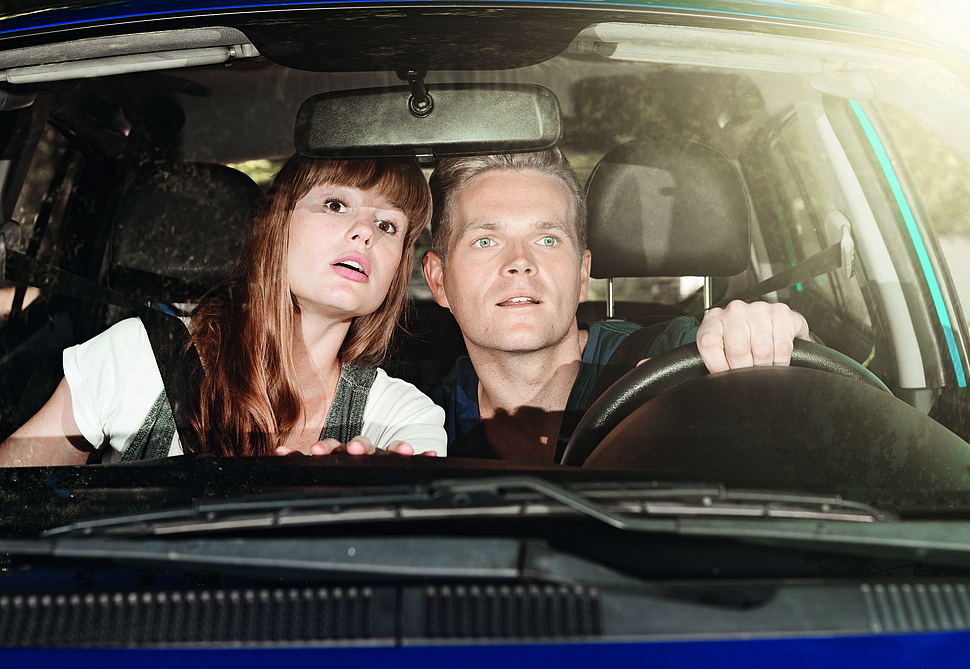 Gaffen Zwei Personen sitzen im Auto und schauen intreressiert aus der Frontscheibe.